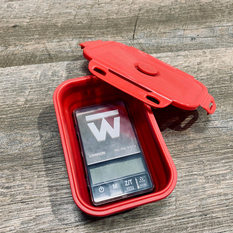 Crimson digital food scale sits in its collapsible red silicone bowl, with the locking cover leaned up against the bowl.