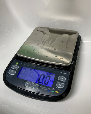 The Truweigh Wave Washdown scale sits in a white porcelain sink and is wet from having just been rinsed off.