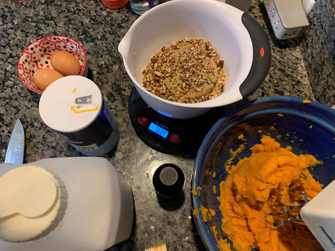 The Truweigh Vortex is weighing a bowl of brown sugar and pecans that will go on top of the sweet potato casserole being prepared in the bowl below the scale. There are other ingredients also scattered in frame on the granite counter.