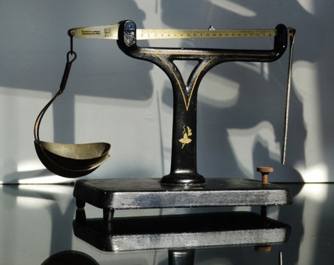 A black iron unequal arm balance sits on a black counter with a shadowy background. 