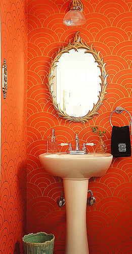 small bathroom with gold and orange wallpaper, round gold mirror, pedestal sink... Beautiful Bathroom Inspiration: Orange Bathrooms from The Bathroom Bliss Blog by Rotator Rod, the original curved shower rod that rotates!