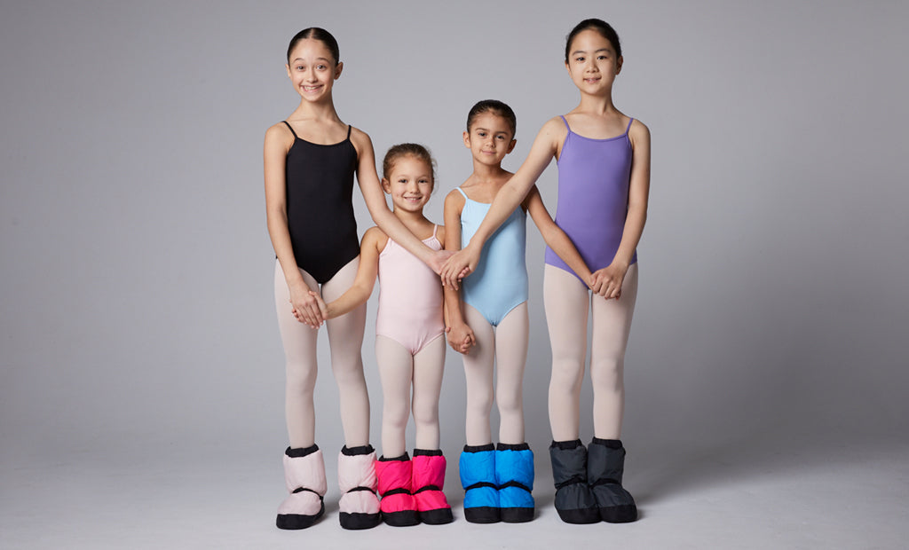 Four young ballet dancers posing together in the studio wearing their Warm Up Booties before ballet class 