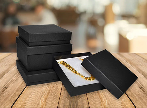 Stack of 3 Black Cotton Filled Boxes with 1 Open Black Box with a Gold Chain All on a Wood Table