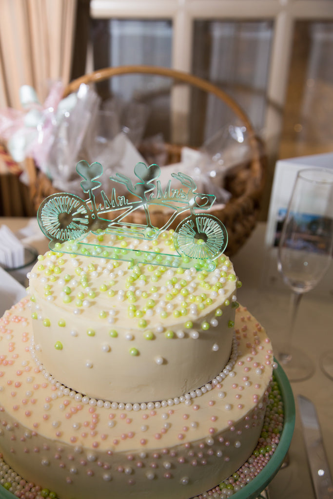 White wedding cake with pale green, tandem bicycle wedding cake topper that says, Mr. and Mrs. at the Chateau Vaudreuil reception venue in Montreal, Quebec.
