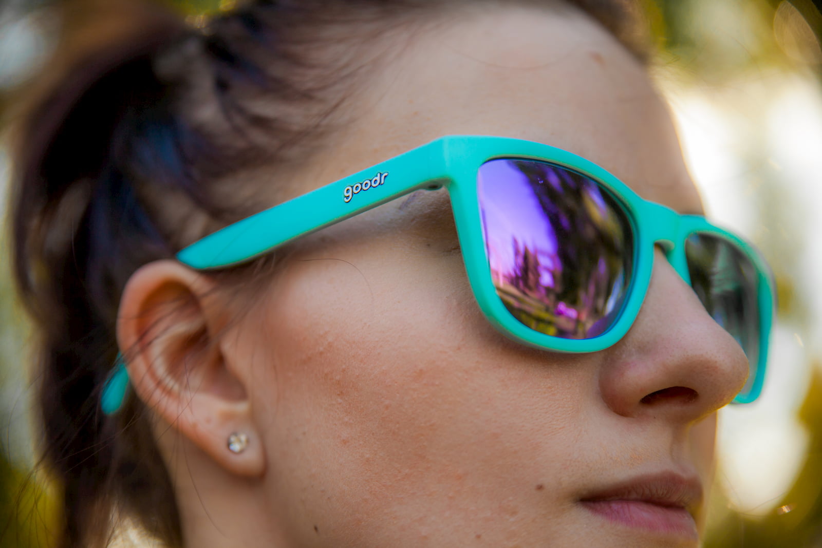 woman wearing teal with mirrored purple lenses goodr sunglasses