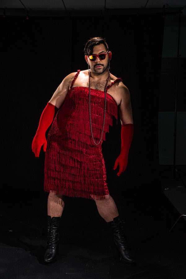Man wearing a roarin' 20's style fringe dress and red gloves and red framed goodr glasses