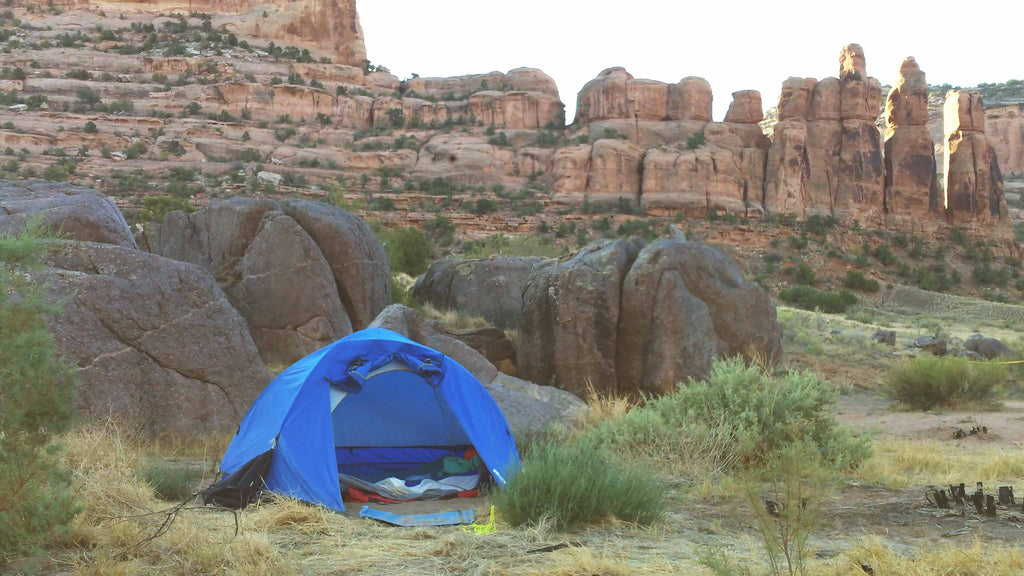 tent pitched on grass in front of rock boulders