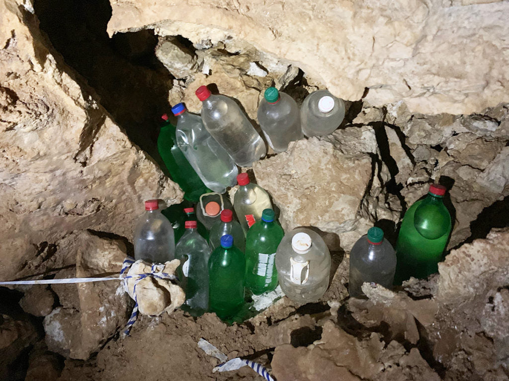 A cache of re-used 2-liter bottles filled with clean water tucked in amongst the rocky crevices of a cave. Photo credit John Waller/Uncage the Soul Productions.