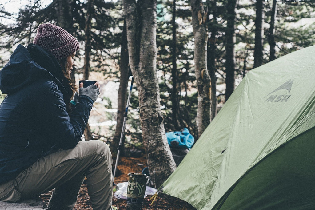 woman sitting outside green tent holding tin mug