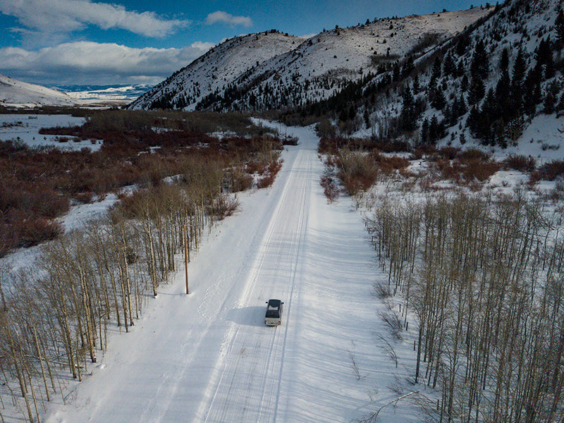 drone shot of a camper van on a snowy road with trees on either side