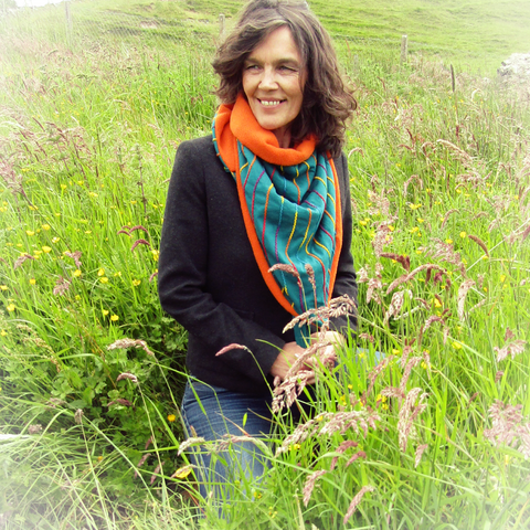 Dark Haired Lady Wearing a Cosy Fleece V-Shaped Teal Green and Orange Neck and Chest Warmer Whilst Kneeling In The Long Grass