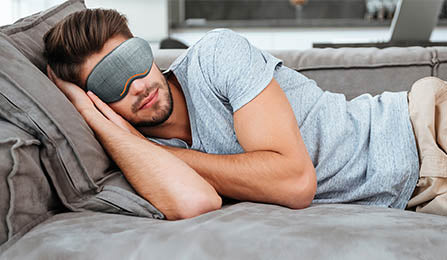 handsome_man_asleep_on_a_sofa_using_a_sleep_mask