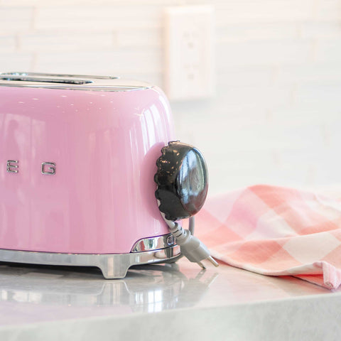 pink smeg toaster on white background with cord storage device