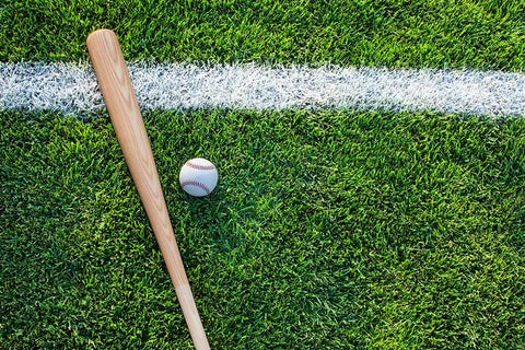 A wood baseball bat, and baseball lying on the grass, with a white stripe going by them.