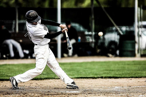 A batter, in a black and white uniform hitting a line drive with a wood baseball bat.