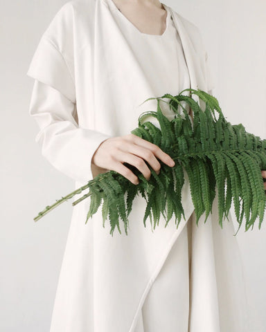 A woman in white holding a bundle of green leaves, for Ivy Leaf Skincare