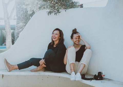 Two women sitting outside with wine, laughing and smiling, for Ivy Leaf Skincare