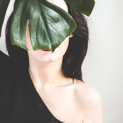 Woman standing behind dark green leaf for Ivy Leaf Skincare, covering face