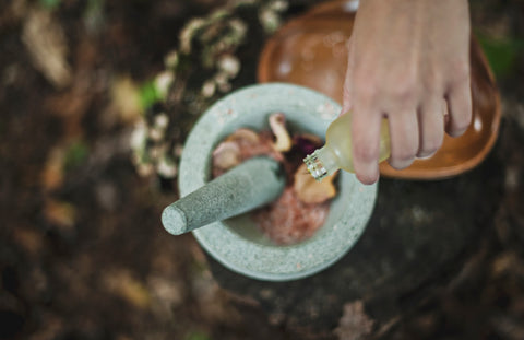 Person pouring elixir into stone bowl of herbs outside, for Ivy Leaf Skincare blog