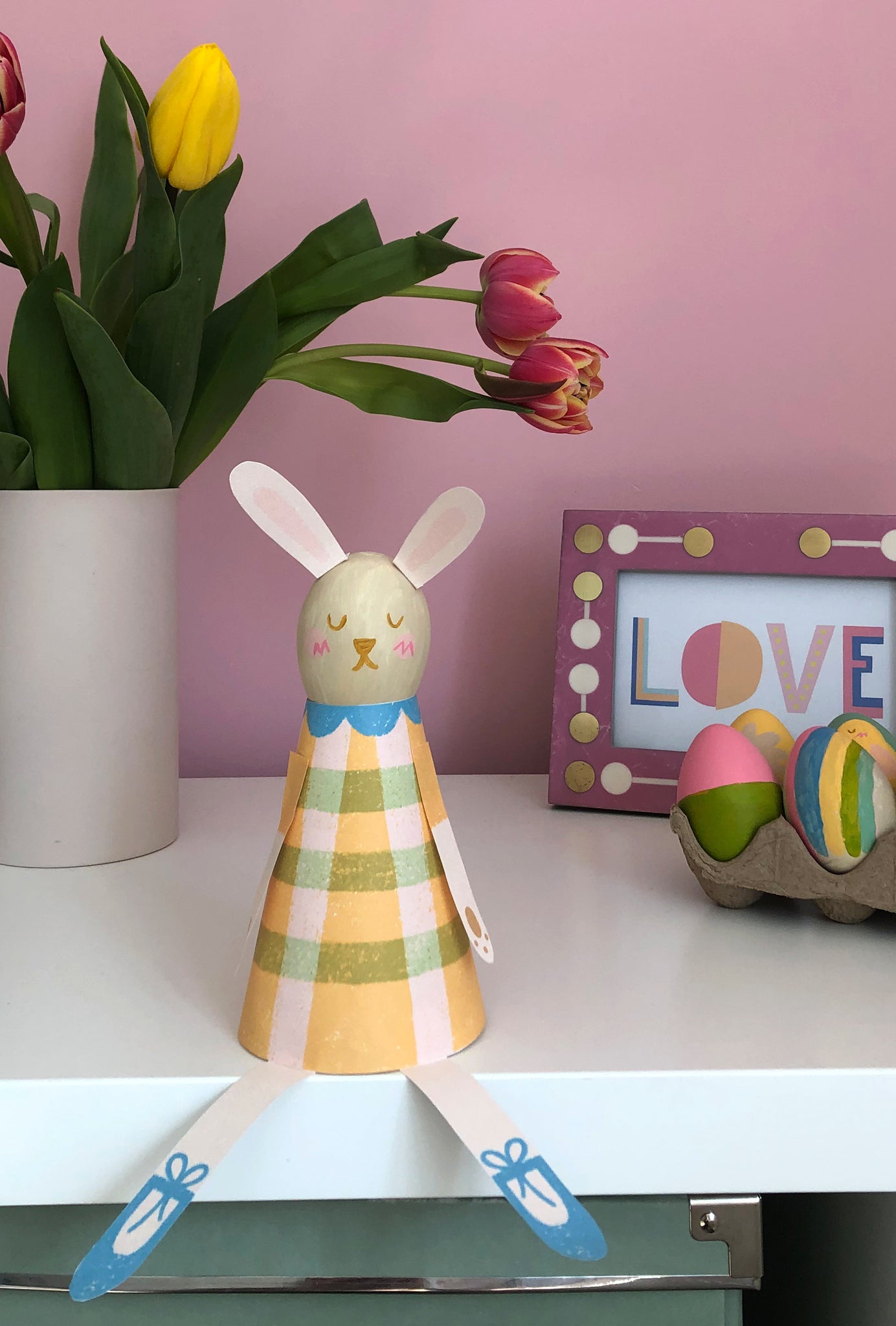 Finished Paper Bunny craft for kids on shelf styled with colourful tulips and painted Easter eggs