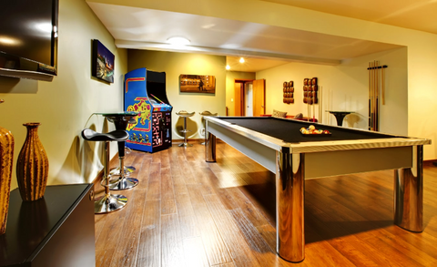 A home game room in a finished basement area with a pool table, wall-mounted television, and Ms. Pac-man arcade machine. 