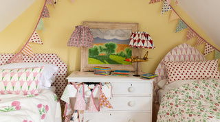 Attic room spilling over with Molly Mahon's hand block printed designs on headboards, quilts, cushions, lampshades, and bunting with two single beds separated by a small chest of draws