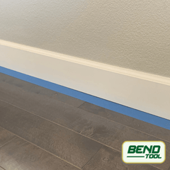 Bend Tool Co. - White profiled baseboard prepped with blue painters tape on hardwood floor