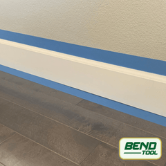 Bend Tool Co. - White profiled baseboard prepped with blue painters tape on hardwood floor and wall.