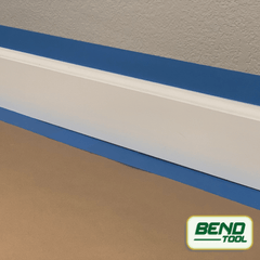 Bend Tool Co. - White profiled baseboard prepped with blue painters tape on hardwood floor and rosin paper