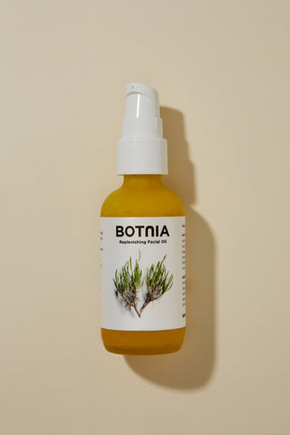 overhead image of botnia's replenishing treatment oil. Glass bottle, with a white pump top and a white label with flowers on it. 