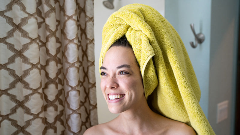 Woman Smiling and Wearing Bright Yellow Towel in Bathroom