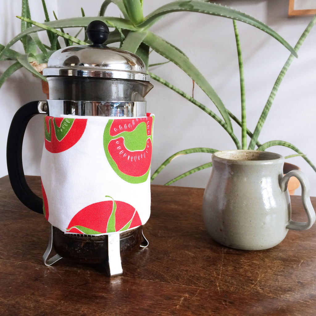 A french press wrapped in a tea towel with a coffee mug sitting next to it