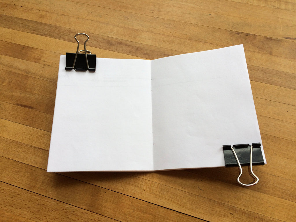 A stack of paper clipped together with binder clips at each end