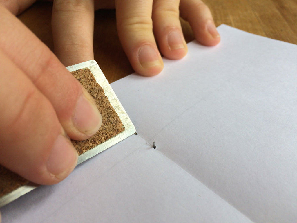 hand pushing over staples with a ruler