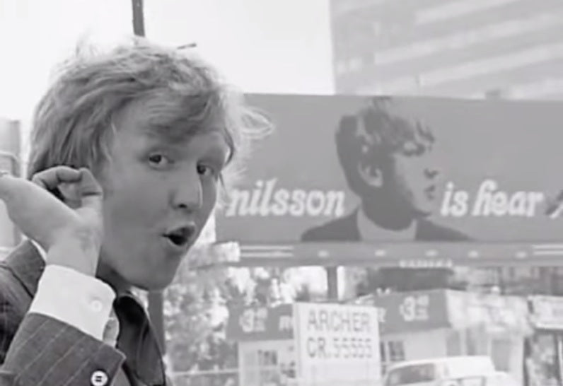 Harry Nilsson poses in front of a promotional billboard