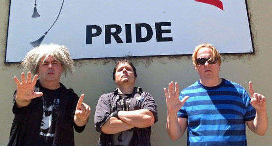 The Melvins stand in front of a sign that says Pride