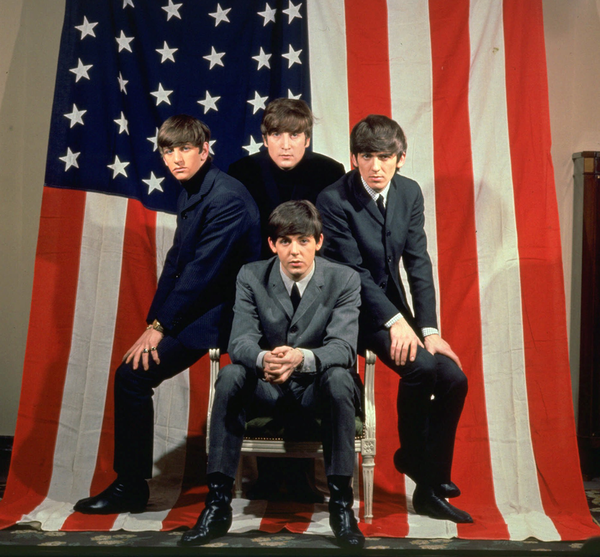 The Beatles pose in front of an American flag in a promotional photo for their 1964 trip to USA