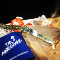 gold vip holographic plastic wristband, blue koozie, and packet of ketchup with some pocket change in the background 