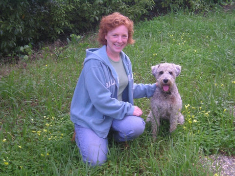 Dog owner poses with white schnoodle in back yard