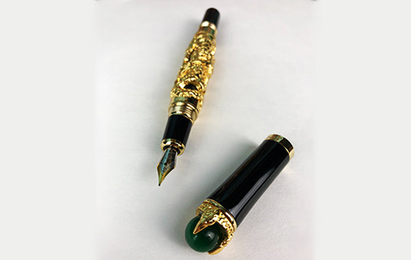 A black fountain pen with gold embellishments around its barrel lying on a sheet of paper with its cap off and lying beside it