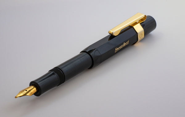 A black fountain pen with gold accents around the nib and cap lying on a plain white surface with its cap posted on its rear end