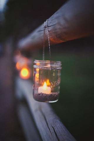 candle in a jar hanging on a wooden fence at dusk