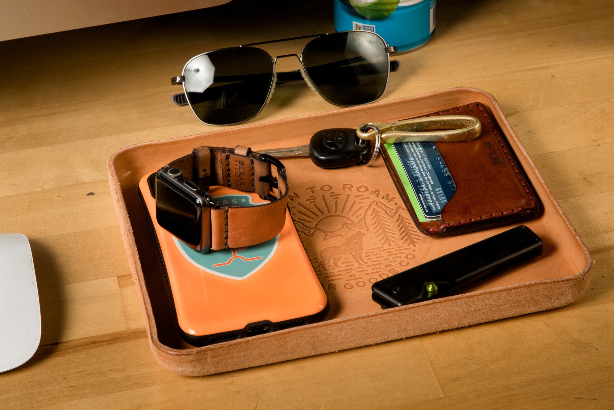 A leather valet tray organizes multiple elements. Orange Phone, Aviator sunglasses, Car Key with brass hook, Apple Watch with leather strap, and a Leather Bexar Goods Wallet