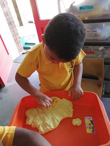 boy playing with yellow stretchy sand in red tray