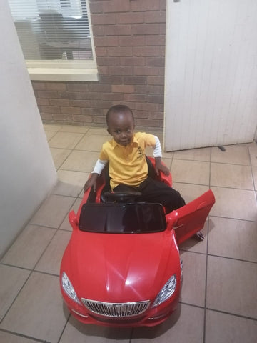 boy in a yellow t-shirt sitting in his red toy car