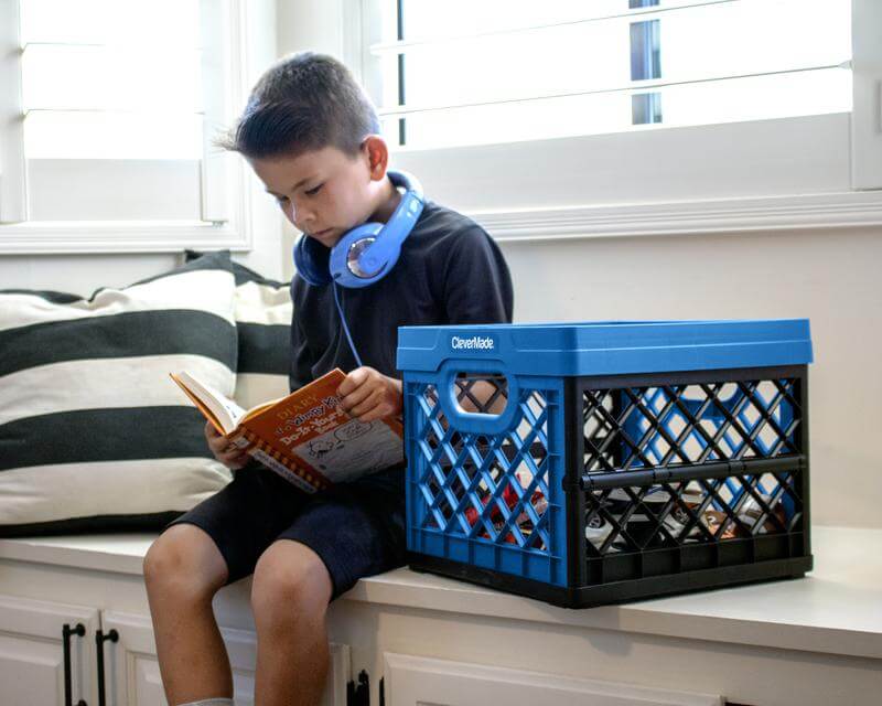 Young boy reading a book next to a CleverCrate® Milk Crate holding books