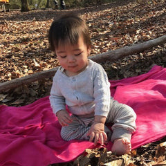 オーガニックコットンのグレーのストライプズボンをはいて、落ち葉の上に座っている幼児