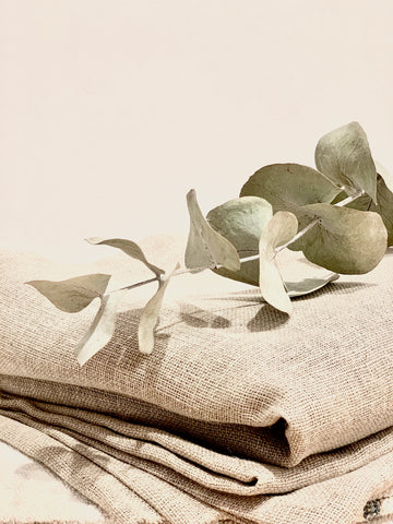 Vocco natural linen fabrics piled with green leaves on top.