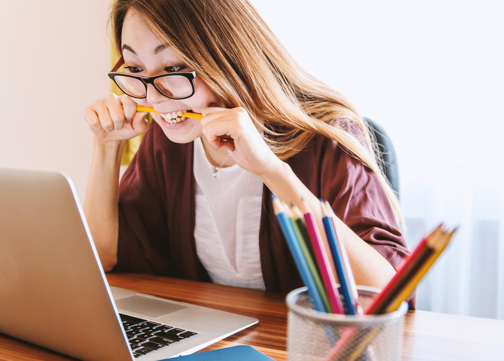 woman with laptop biting pencil