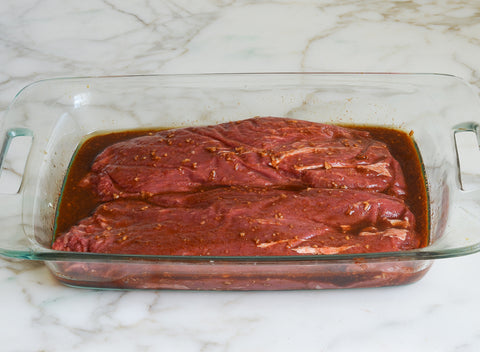 Photo of the two 1-pound pieces of flat iron steak side by side in the spices inside the pyrex dish.